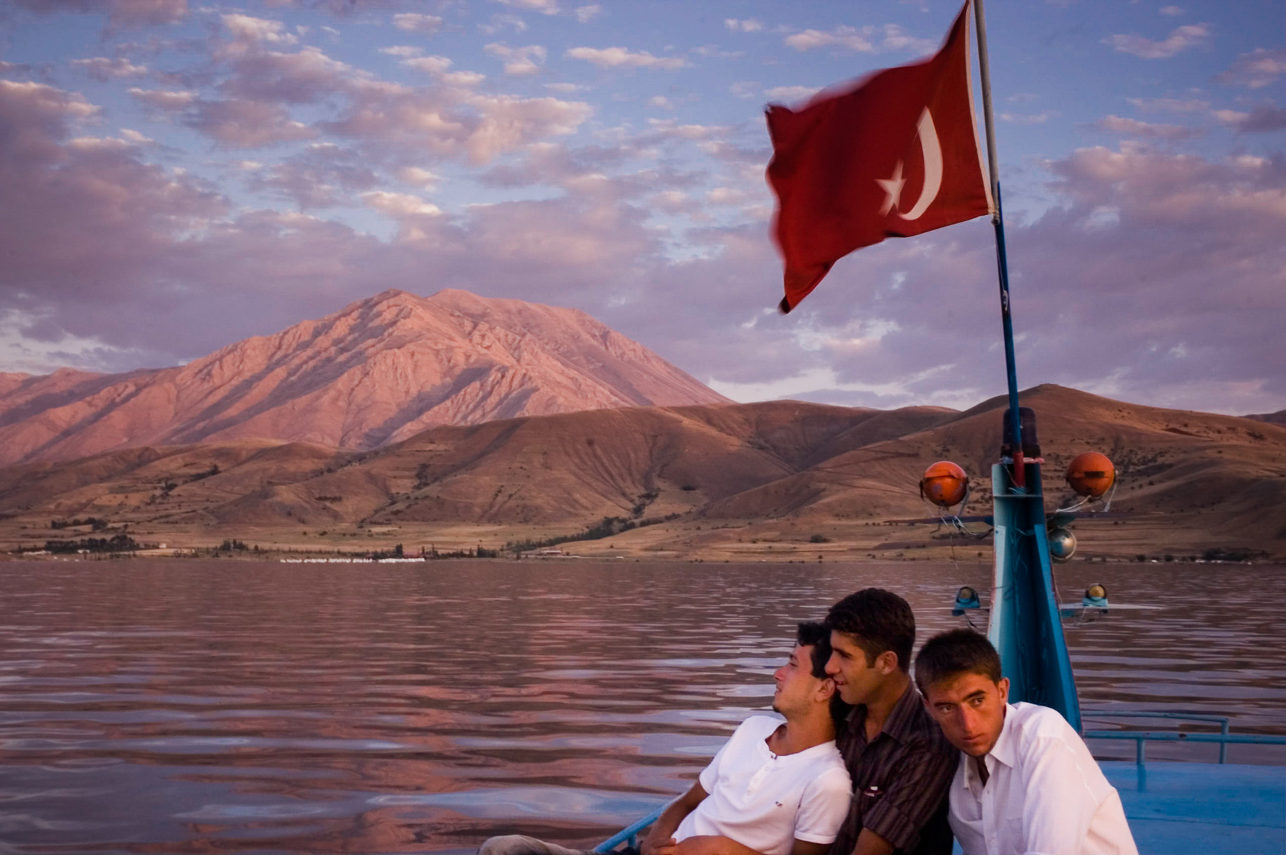Young Kurdish men on boat on Van Lake under Turkey flag, Akdamar Island Turkey. 