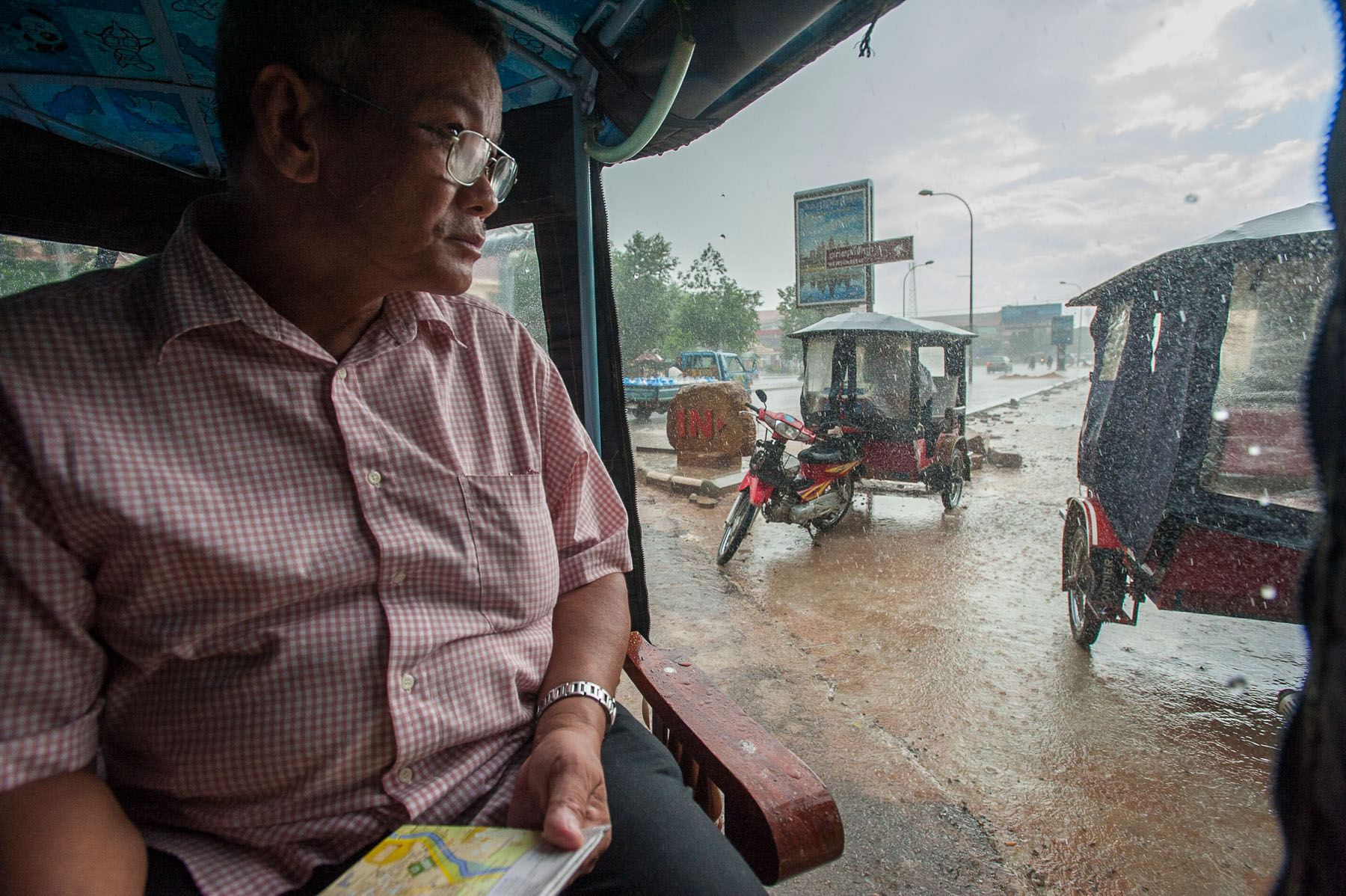 Man sitting in tuk tuk in rain, Siem Reap Cambodia. 