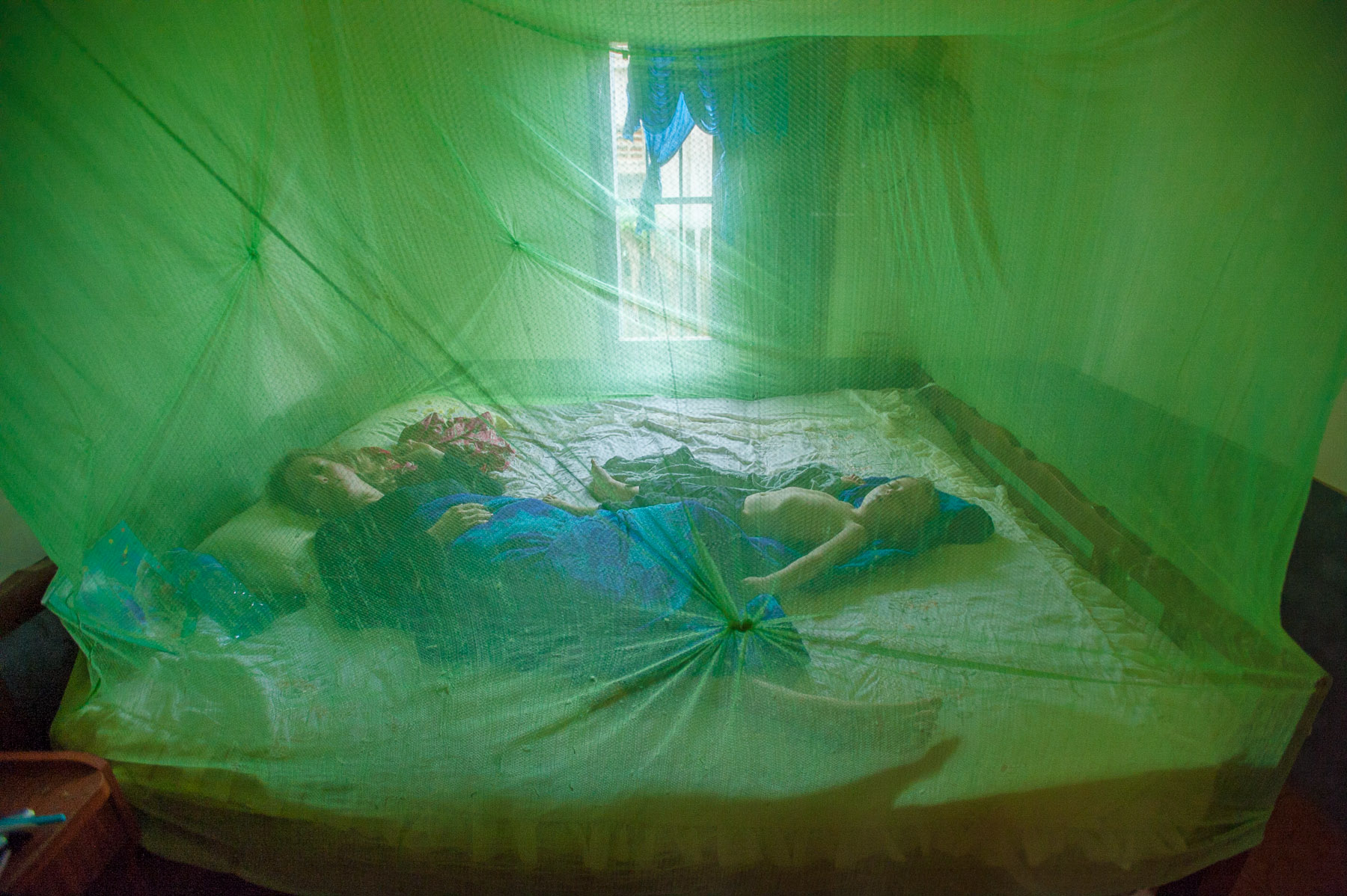 Mother and son sleeping under mosquito net, remote village Cambodia.