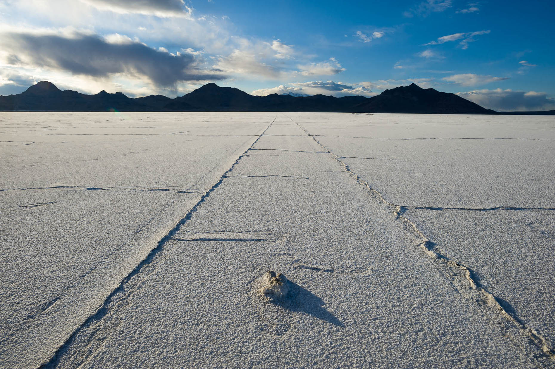 Receding tire track lines in Salt Flats, Utah with blue sky and mountains on horizon. 