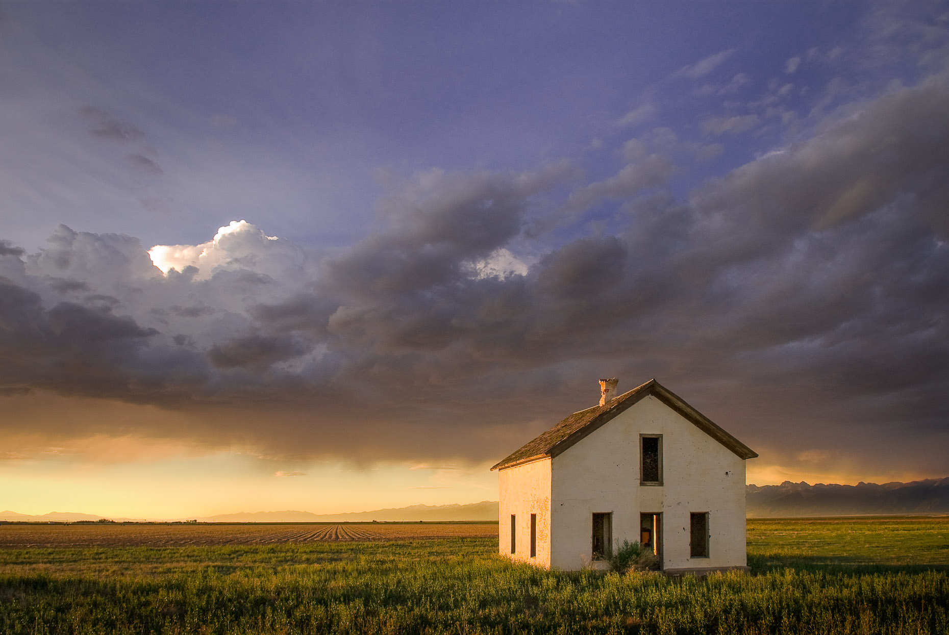 Abandoned small farm house in green field at dramatic sunset and rain storm. 